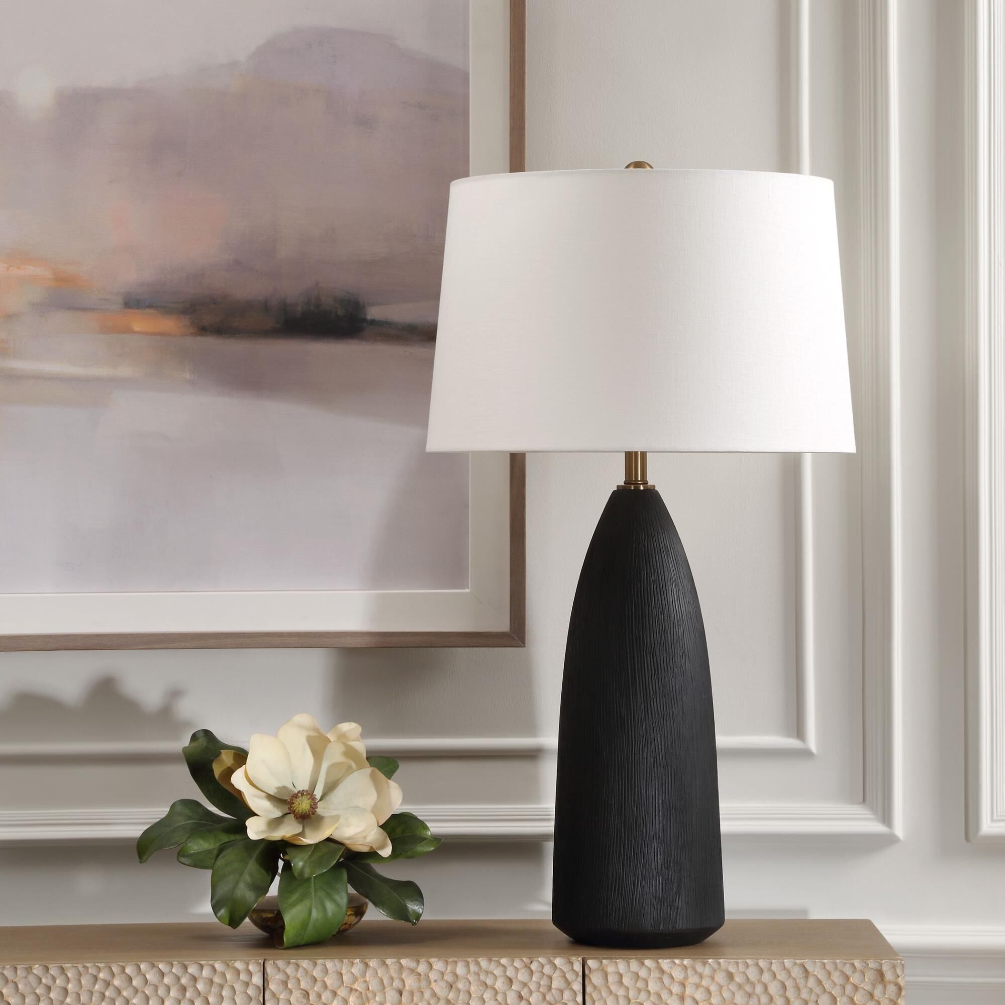Shown in The Jett Table Lamp Showcases A Matte Black Ceramic Base With Organic Texturing, Accented With Plate finish and Round Hardback shade