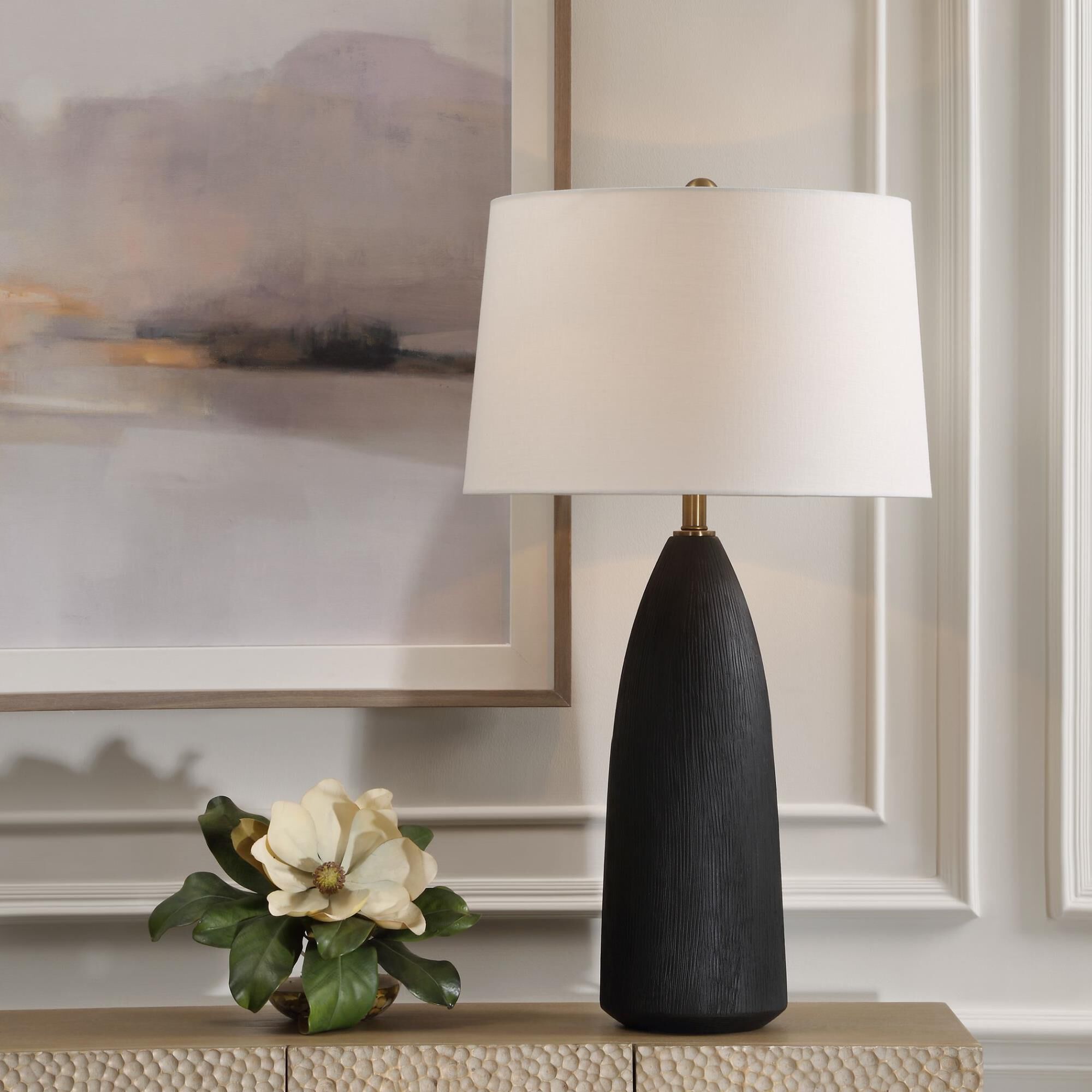 Shown in The Jett Table Lamp Showcases A Matte Black Ceramic Base With Organic Texturing, Accented With Plate finish and Round Hardback shade