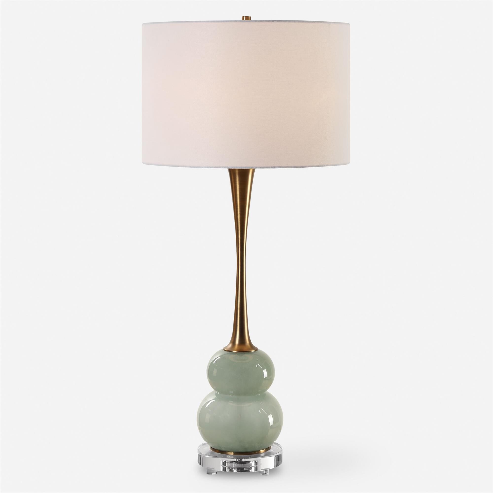 Shown in The Sanctuary Table Lamp Features A Curvy, Greenish-Gray Glass Body Paired With A Fluted Style Neck  finish and Round Drum Hardback shade